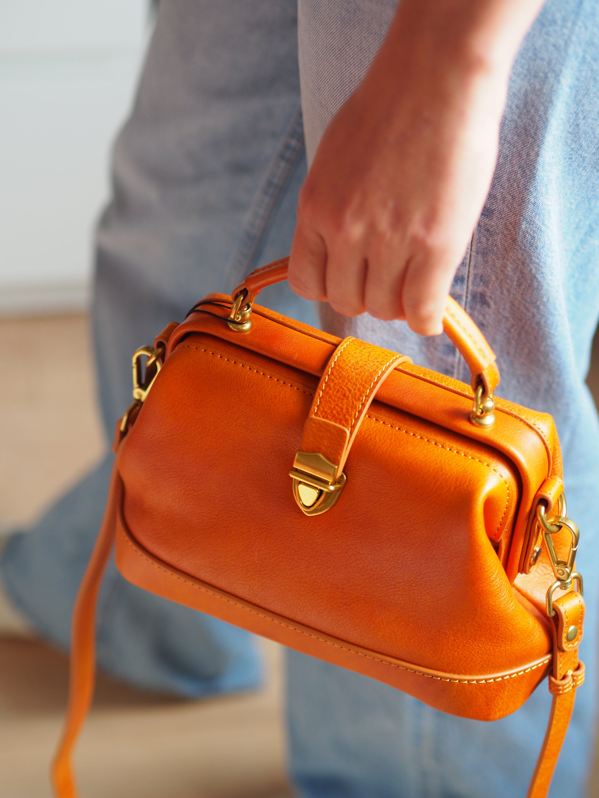 Orange handbag with gold accents held by a person wearing blue jeans.