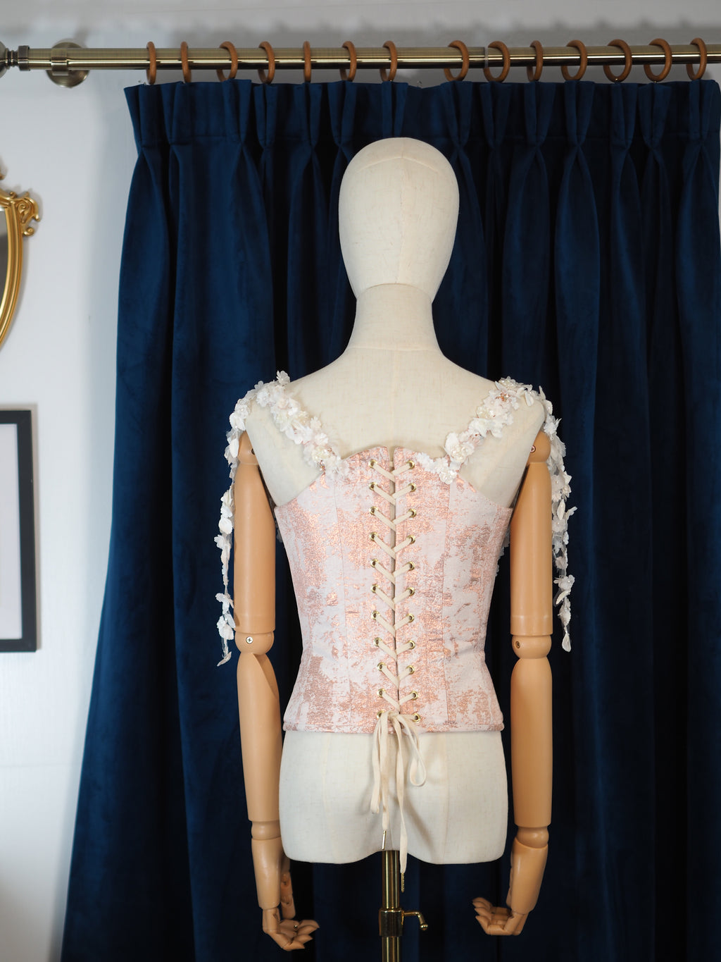 Mannequin wearing a pink lace dress with floral details against a dark blue curtain.