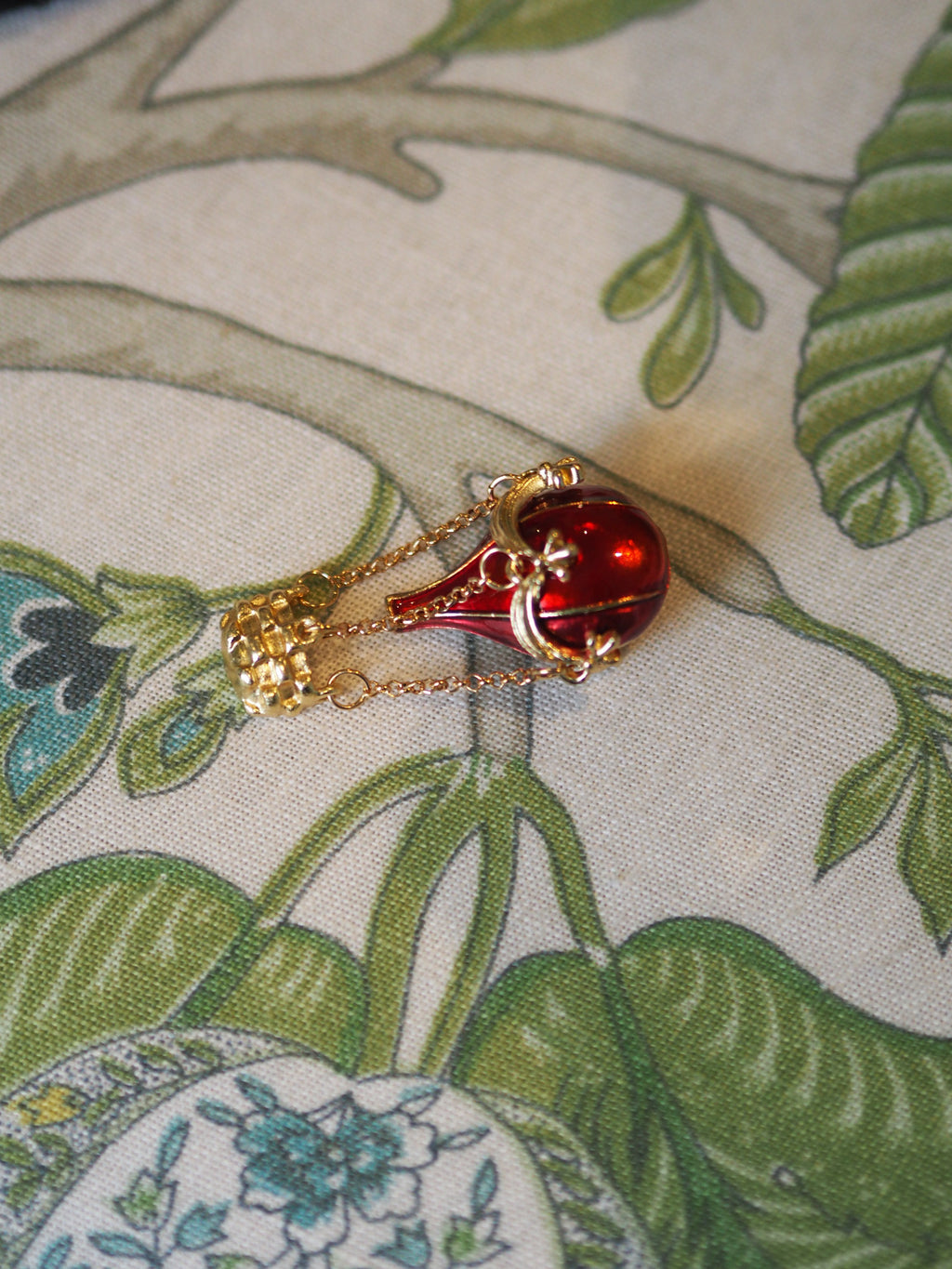 Red teardrop-shaped pendant with gold chain on a floral fabric background