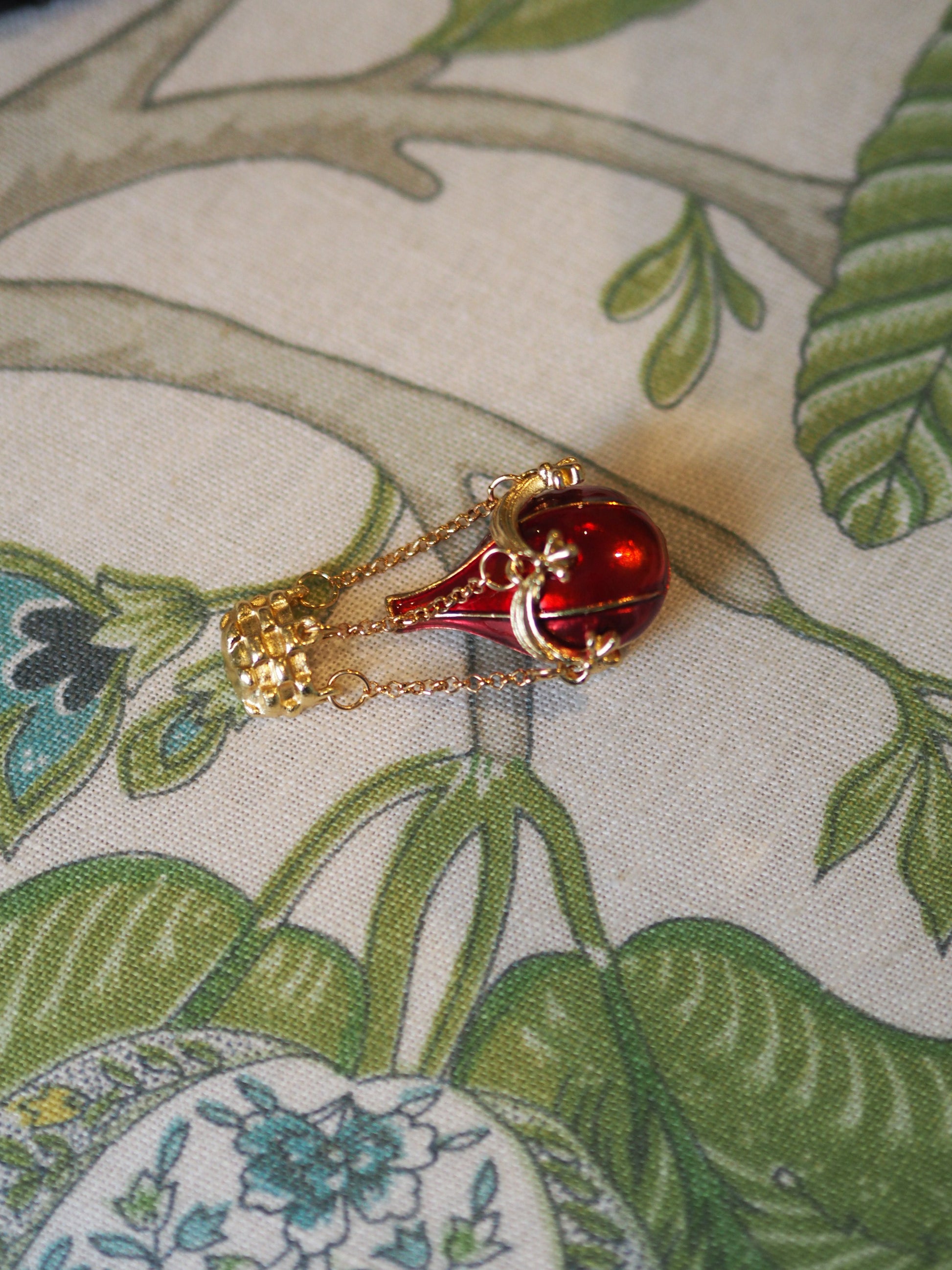 Red teardrop-shaped pendant with gold chain on a floral fabric background
