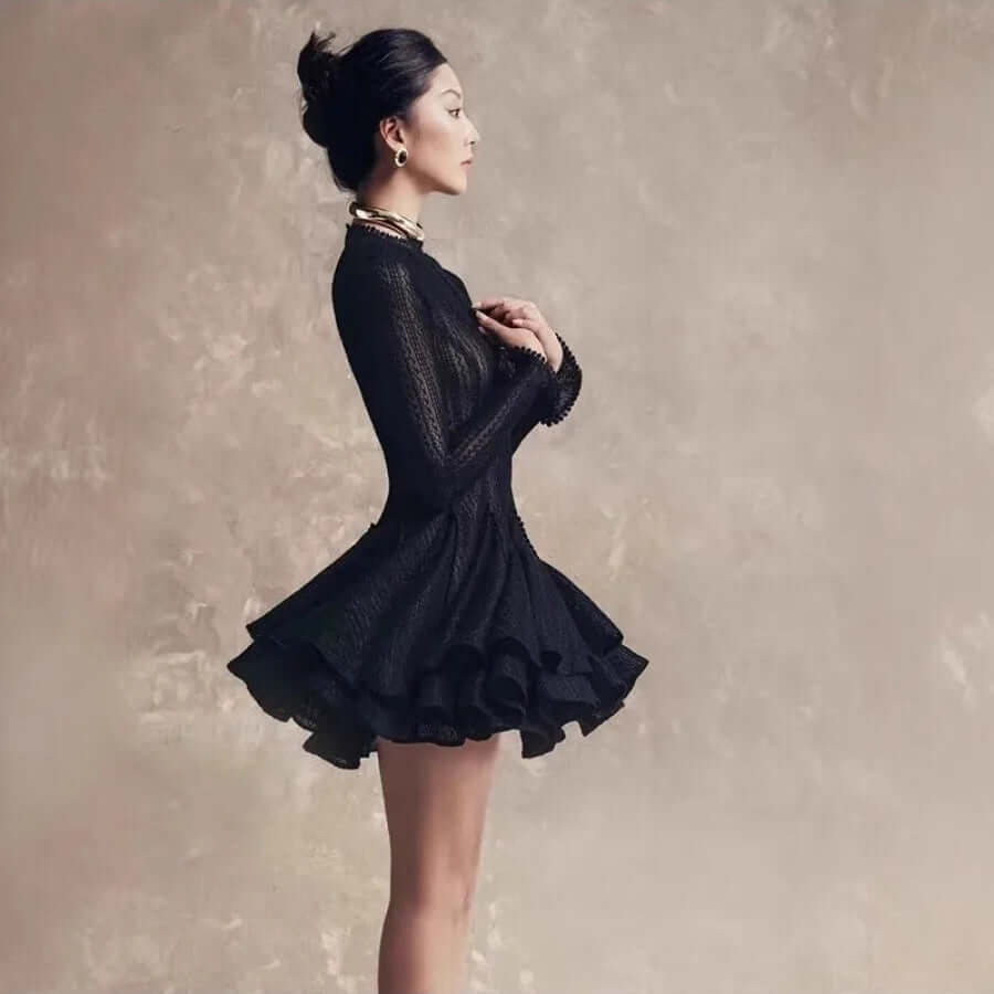 an asian womanphotographed sideways wearing a short blak dress with long sleeves and a full skirt 