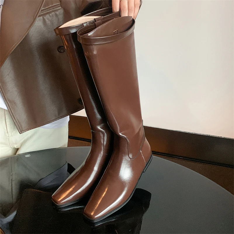 Brown knee-high boots being worn with a person partially visible in the background.