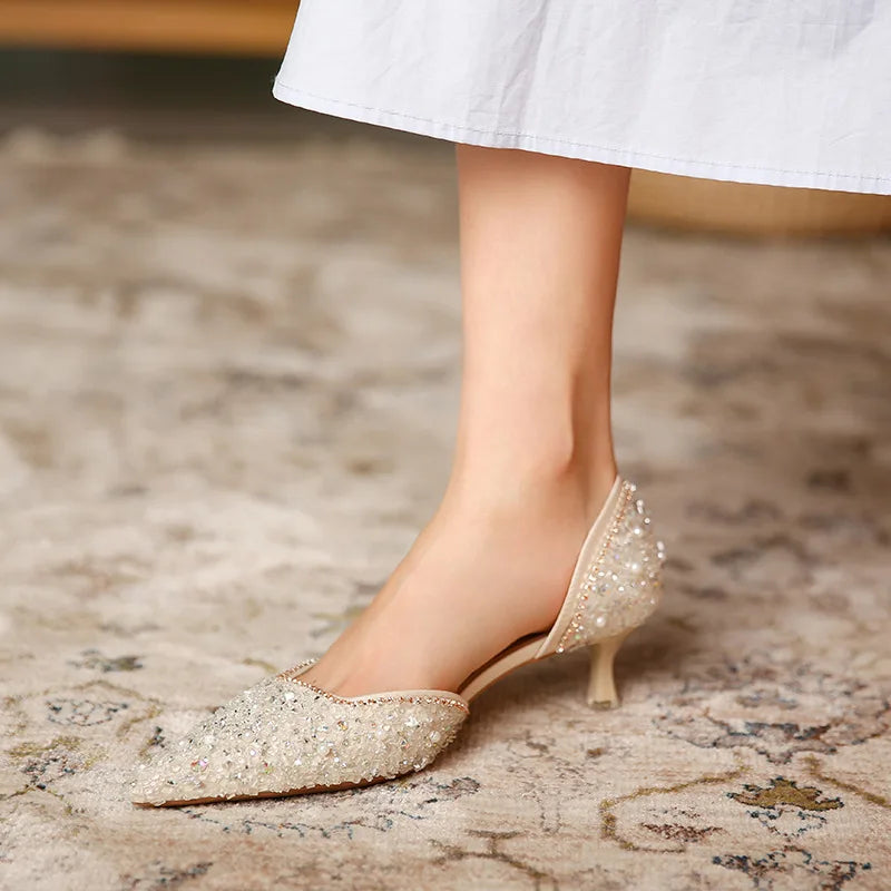 Sparkly high-heeled shoes worn with a white skirt on a patterned carpet.
