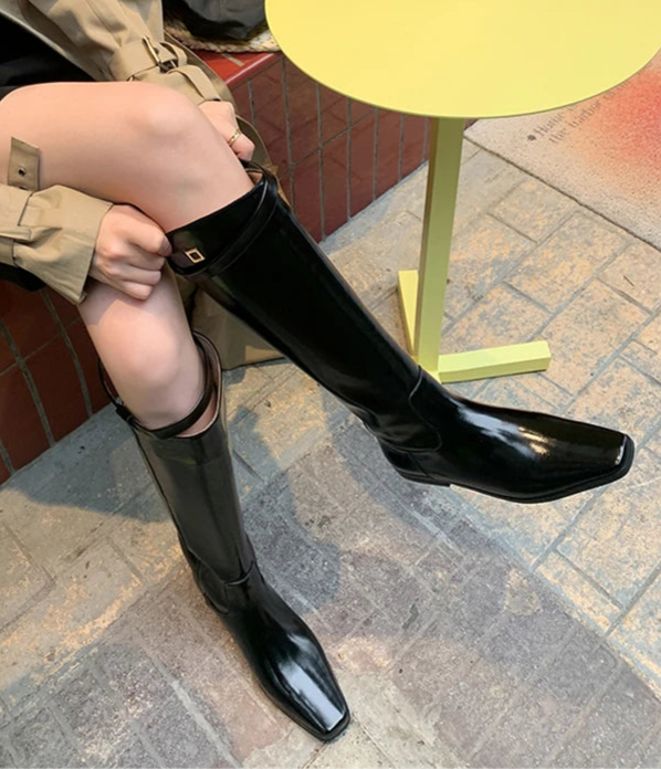 Person wearing black knee-high boots sitting on a yellow stool with a patterned floor.