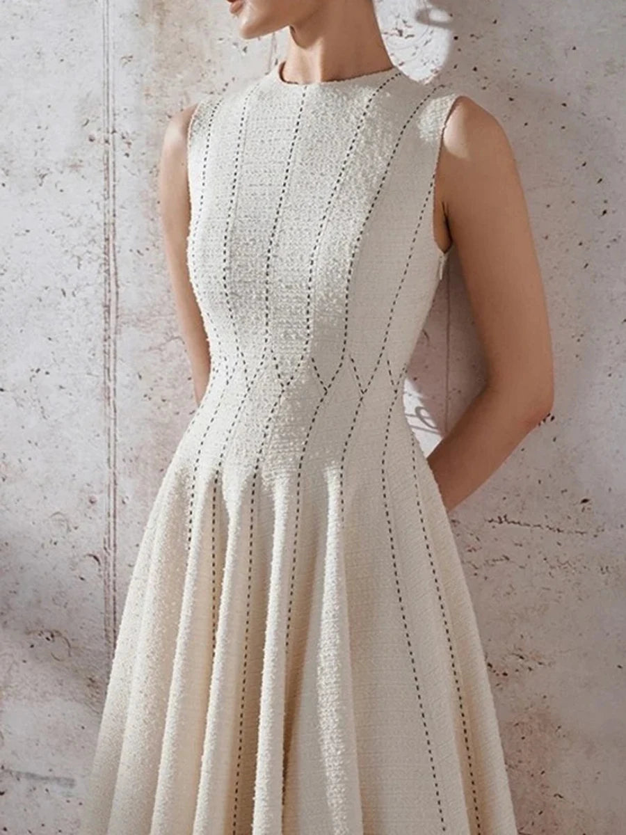 White sleeveless dress with intricate detailing on a textured wall background