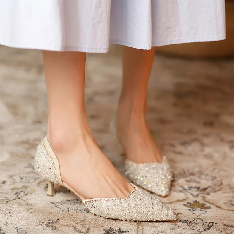 Sparkly high-heeled shoes worn with a white skirt on a patterned carpet.