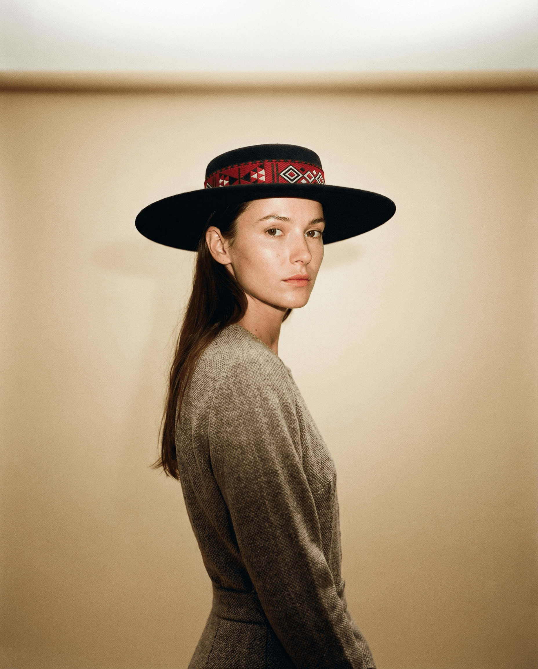Woman wearing a wide-brimmed hat with a patterned band against a beige background