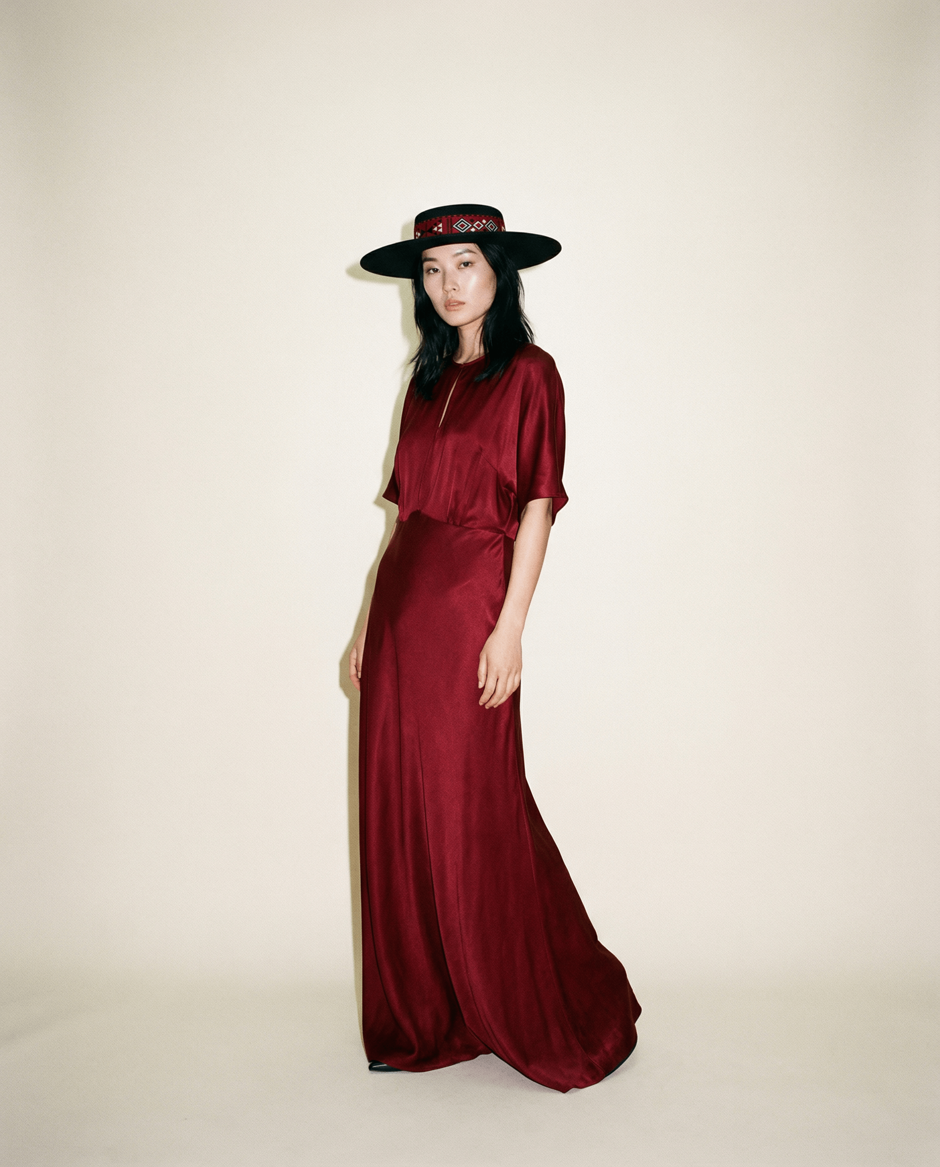 Woman wearing a burgundy dress and black hat on a plain background